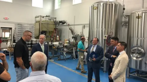 A group of men talking in front of brewery equipment.
