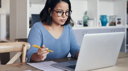 Woman in glasses at lap top working and taking notes.