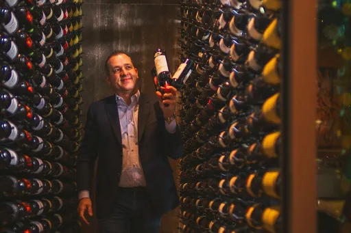 Viron Rondos holding several bottles of wine in a wine cellar