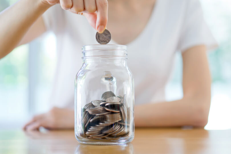 A woman drops a coin into a coin jar.