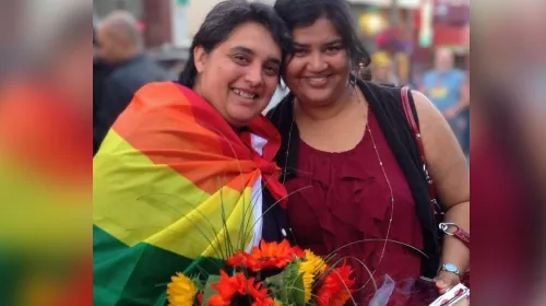 Two women posing for a picture wrapped in a rainbow flag. 