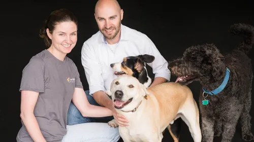 Paul and Laura Abbott smiling while crouched beside multiple dogs.