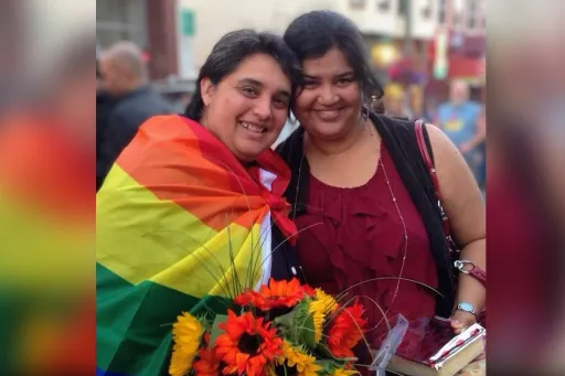 Two women posing for a picture wrapped in a rainbow flag. 