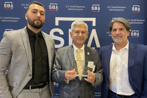 Eduardo Crespo wearing a suit and smiling while holding his Minority Owned Small Business of the Year award.