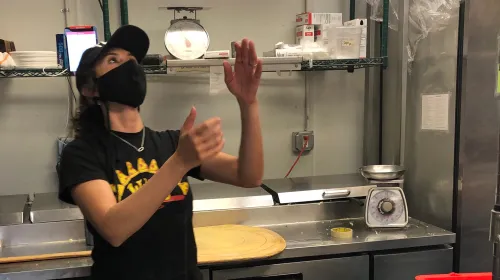 Small business owner Melissa Maese Goldberg flipping pizza dough for her pizza shop