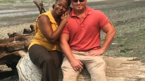 Makieda Hart and husband sitting on a rock in front of the ocean