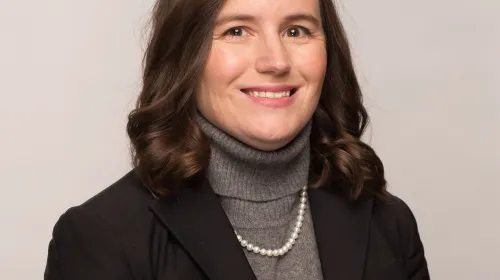 A picture of Sarah Scala wearing a sweater, blazer, and pearls, smiling at the camera.