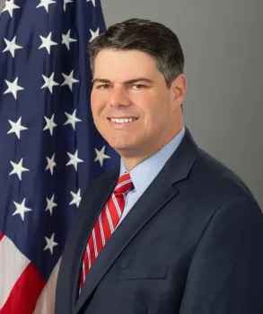 A picture of Mike Vlacich smiling with an American flag in the background.