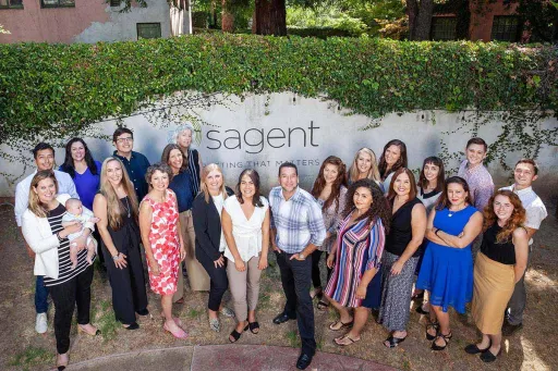 Group photo of the Sagent team in front of the light gray etched stone sign at their new historic headquarters building.