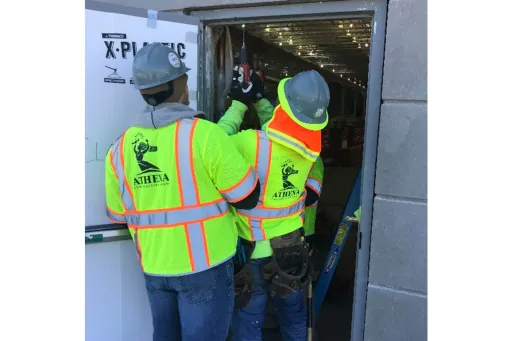 Two Athena employees working on an exterior doorway of a building.