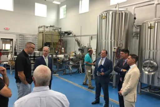 A group of men talking in front of brewery equipment.