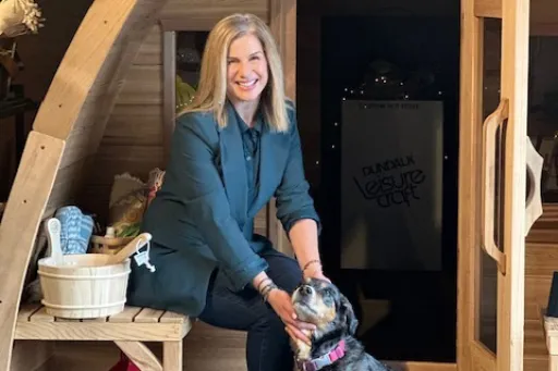Woman owned small business owner sits outside the sauna while petting their dog